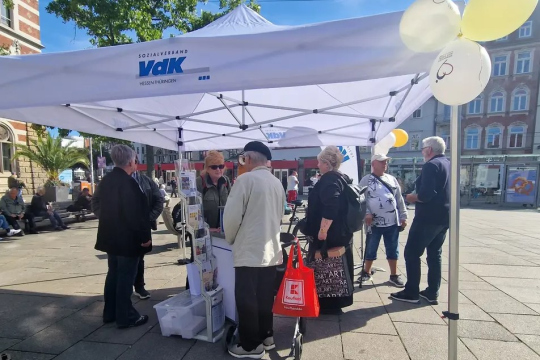 Mehrere Personen an einem VdK-Infostand bei strahlenden Sonnenschein. 